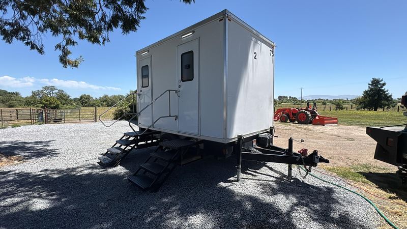 Restroom trailer on a gravel ranch pad with fields behind it